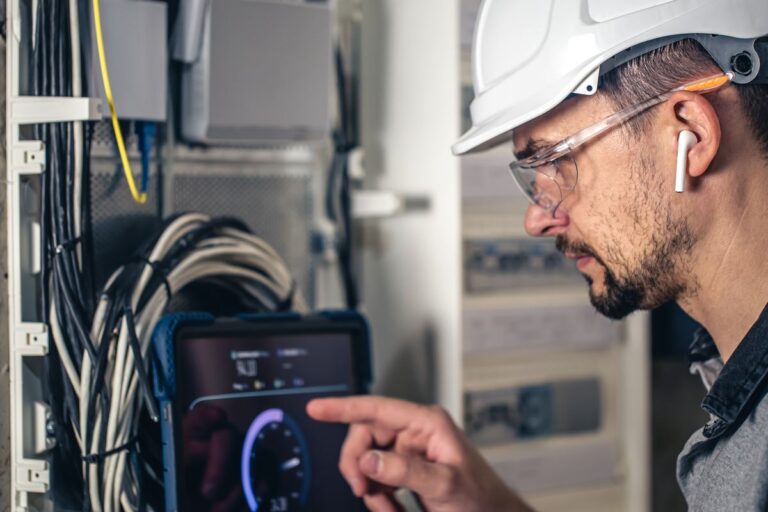 Man, an electrical technician working in a switchboard with fuses. Installation and connection of electrical equipment. Professional uses a tablet.